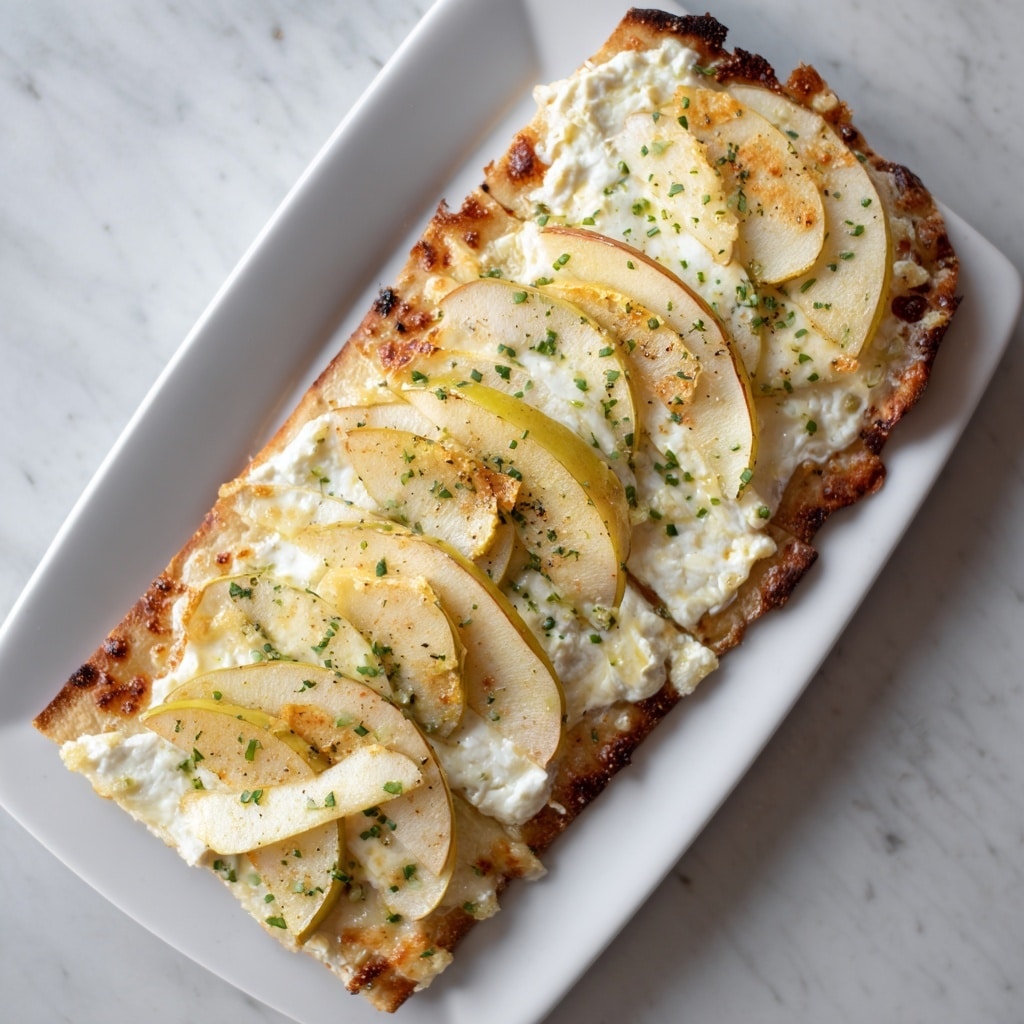 A flatbread with a golden-brown, slightly crispy crust as the base, topped with creamy white melted brie cheese spread evenly across the surface. On top of the cheese are thin, slightly browned slices of pale yellow apple arranged in a scattered pattern. The flatbread is sprinkled with bits of green herbs, adding flecks of color and texture. The flatbread rests on a white plate placed on a white marbled surface. Photo taken with an iphone --ar 4:5 --v 7