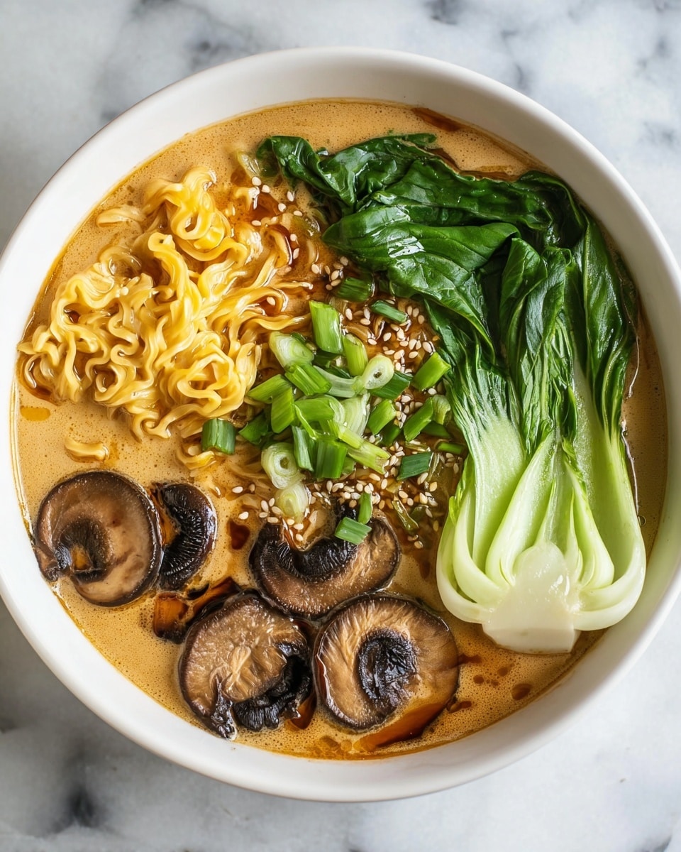 A white bowl filled with creamy light brown broth covers the bottom layer, topped with yellow cooked curly noodles spread on one side. On top of the noodles are small pale sesame seeds and a drizzle of tan creamy sauce creating a pattern near the edge. Next to the noodles, there are fresh chopped bright green scallions scattered. Three thick slices of dark brown mushrooms with lighter inner parts lie beside the scallions. A whole leaf of dark green bok choy with a white stem rests on the broth's surface opposite the noodles and mushrooms. The bowl is set on a white marbled textured surface. photo taken with an iphone --ar 4:5 --v 7