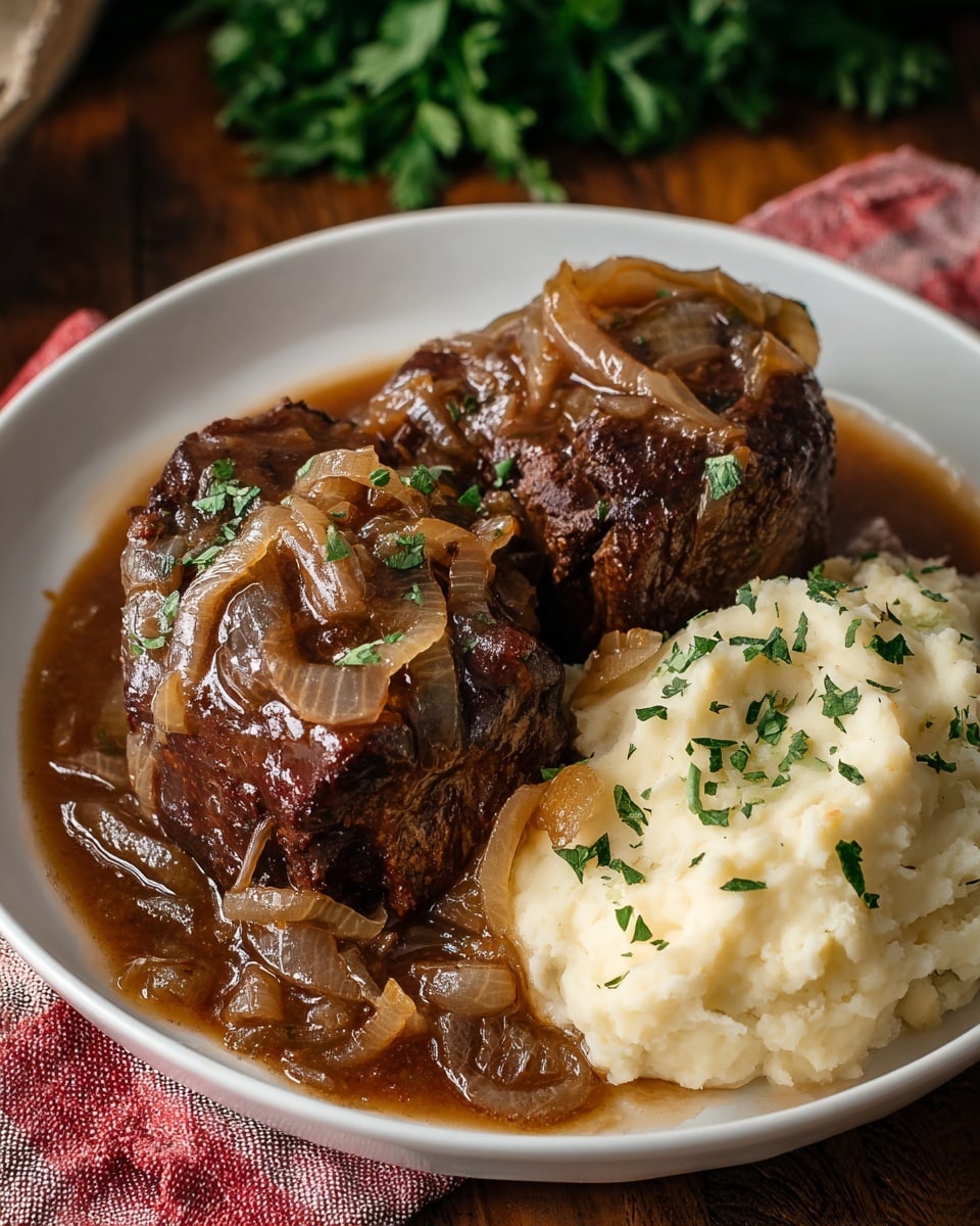 A white plate holds two large pieces of dark brown braised beef covered with chunky, translucent cooked onions and a glossy brown sauce, garnished with small green herbs. To the side is a creamy, light beige mashed potato mound sprinkled with small green herb pieces. The plate rests on a white marbled surface next to a red and white striped cloth with some green leafy herbs blurred in the background. Photo taken with an iphone --ar 4:5 --v 7