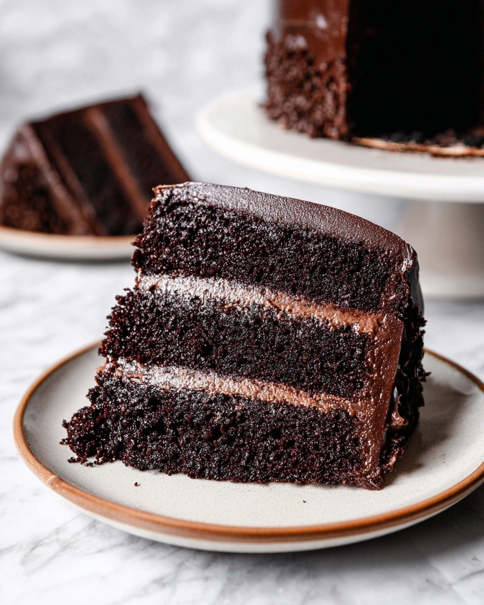 The image shows a slice of chocolate cake with three thick, dark brown layers of moist cake separated by two smooth, lighter brown chocolate cream layers. The cake slice is placed on a white plate with a brown rim, and the cake has a glossy dark chocolate frosting covering the sides and top. In the background, there is a blurred second slice of the same cake on a white plate. The scene is set on a white marbled surface. photo taken with an iphone --ar 4:5 --v 7