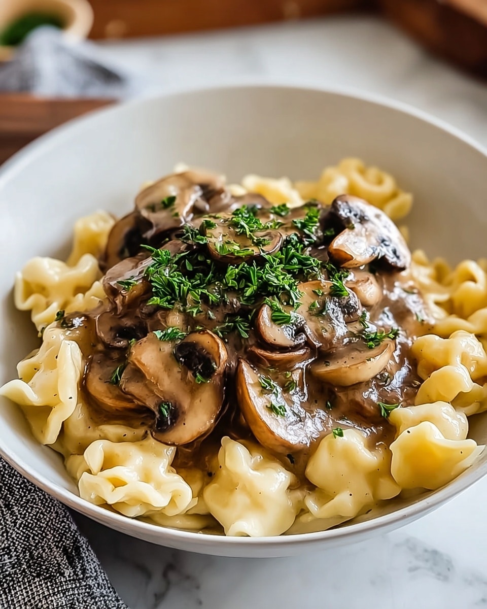 A white bowl holds three layers of food: the bottom layer is creamy, pale yellow pasta with a soft, uneven texture; the middle layer is a glossy, brown mushroom sauce with visible sliced mushrooms that look tender and juicy; the top layer is a sprinkle of fresh, finely chopped green herbs, adding a pop of color. The bowl sits on a white marbled surface, with a gray and white cloth partly visible at the edge. The lighting is soft, making the food look warm and inviting. photo taken with an iphone --ar 4:5 --v 7