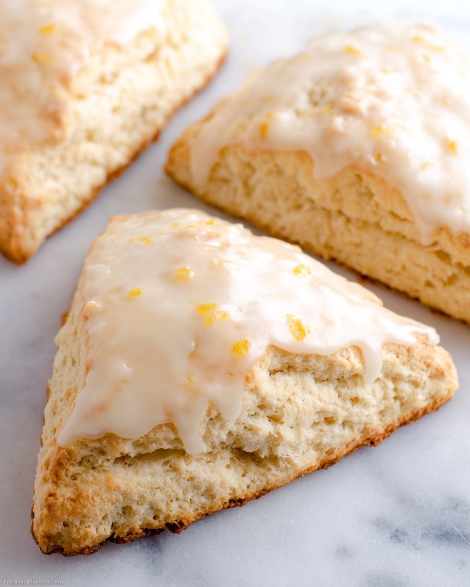 The image shows three large triangular scones arranged close together on a white marbled surface. Each scone has a light golden-brown crust and a soft, fluffy interior with a pale tan color. The top layer of each scone is covered in a smooth, thick glaze that is creamy white with small orange specks scattered throughout. The glaze adds a glossy texture to the scones, contrasting with their slightly crumbly and rustic edges. The focus is on the front scone, with the others gently blurred in the background. Photo taken with an iphone --ar 4:5 --v 7