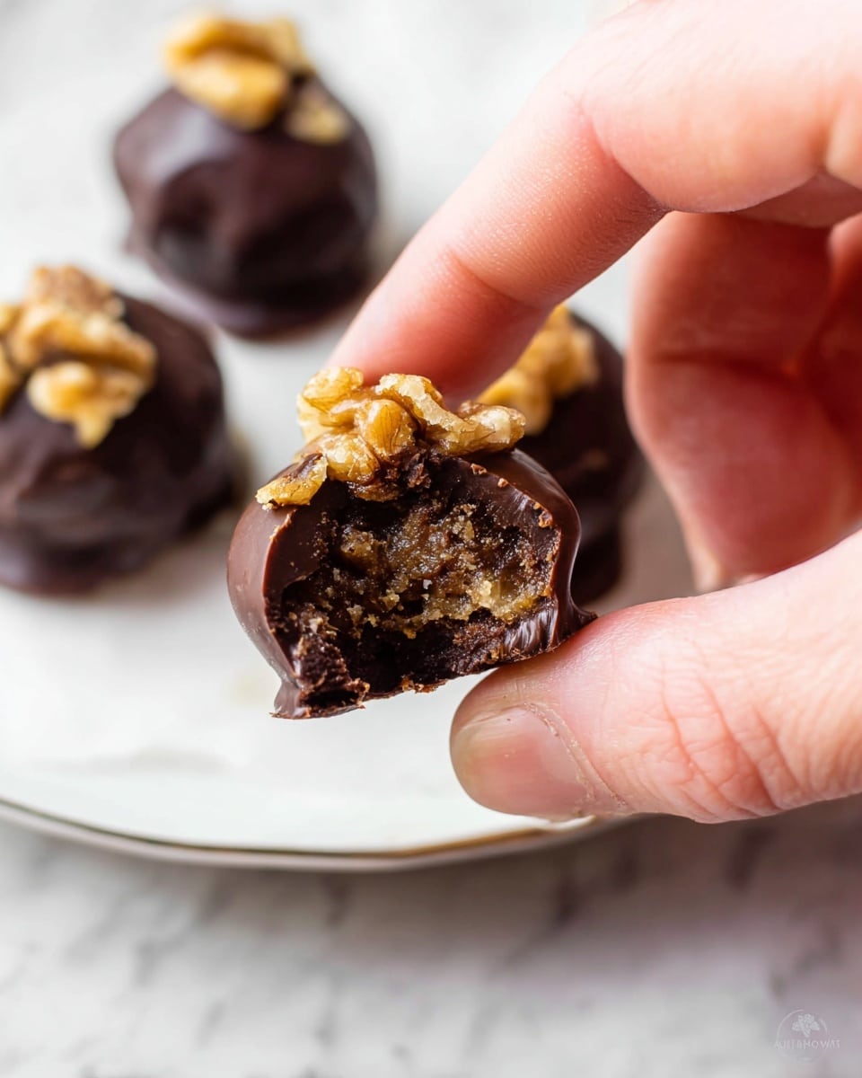 The image shows three small, round treats on a white plate with a slightly raised edge, placed on a white marbled surface. Each treat has two main layers: the outer dark brown chocolate coating with a smooth, shiny texture and a slightly uneven base where the chocolate pools, and a topping of irregular light brown walnut pieces with a rough texture placed on top. The treats are spaced apart, with one in the foreground and two slightly blurred in the background, showing depth in the image. Photo taken with an iphone --ar 4:5 --v 7