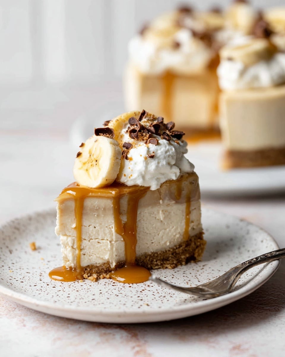 A slice of creamy cheesecake with three visible layers rests on a white speckled plate. The bottom layer is a dense, crumbly light brown crust. The middle layer is a thick, pale beige cheesecake with a smooth texture. On top, slices of banana are placed under a dollop of white whipped cream, sprinkled with small chocolate curls. Golden caramel sauce drips down the sides of the cheesecake onto the plate. A small fork lies next to the slice. In the blurry background, the rest of the cheesecake is on a white plate, sitting on a white marbled surface. photo taken with an iphone --ar 4:5 --v 7