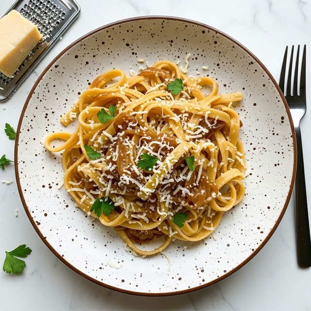 A white speckled plate holds a serving of creamy pasta with caramel-colored onion sauce mixed throughout the long, flat noodles. The pasta sits slightly twisted in the center of the plate, topped with finely grated white cheese and small green parsley leaves scattered evenly over the dish. The edges of the plate show dark brown speckles, adding a rustic touch. The plate rests on a white marbled surface, with a piece of hard cheese and a metal grater to the left, and a black fork to the right. Light shines softly on the pasta, highlighting the smooth texture of the sauce and the shine on the noodles. photo taken with an iphone --ar 4:5 --v 7