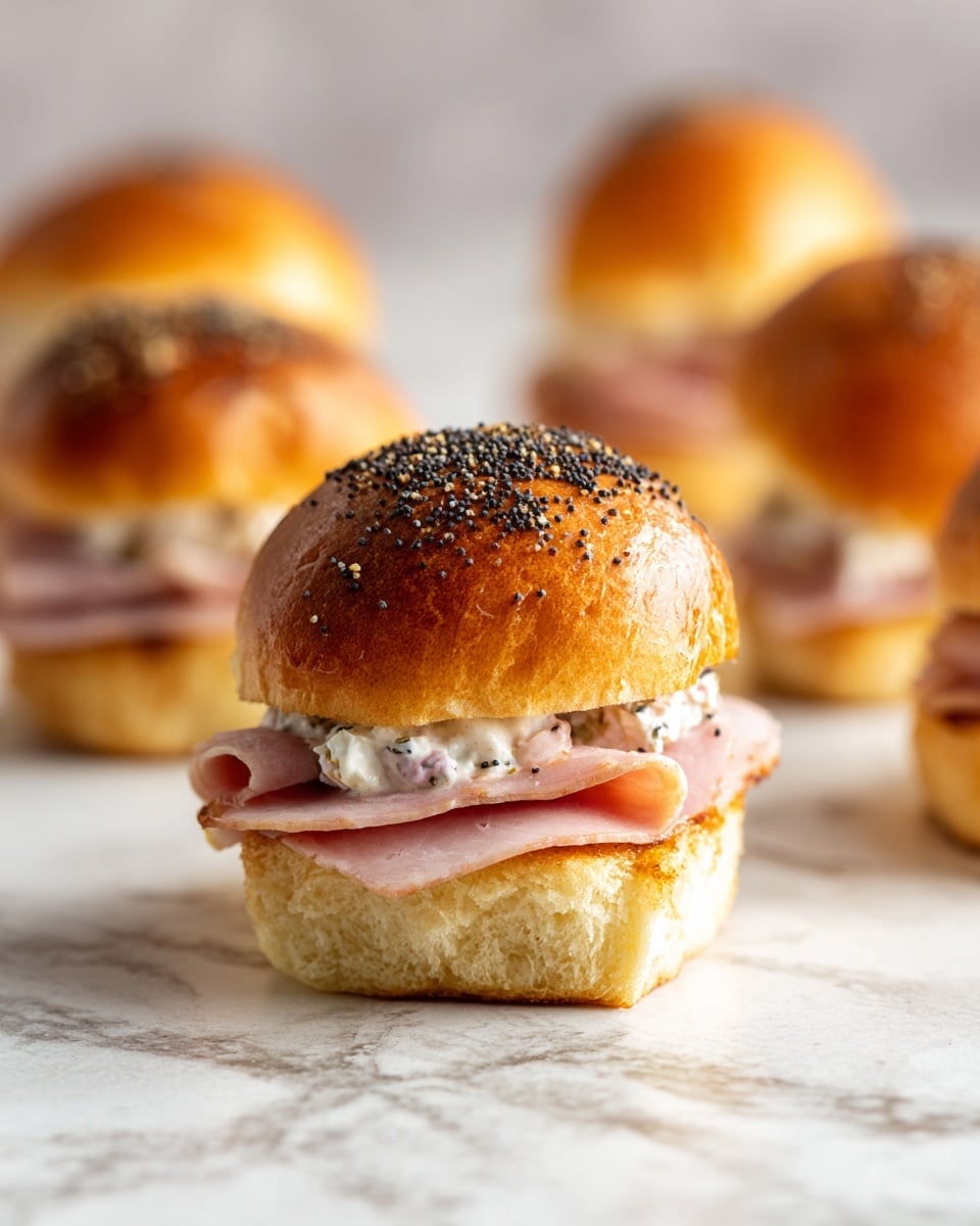 The image shows a close-up of a slider sandwich with three visible layers. The top layer is a golden brown, shiny bun sprinkled with small black poppy seeds, giving it a slightly textured look. Below the bun is a thin layer of melted light yellow cheese, followed by a pale pink slice of deli meat. The bottom layer consists of a creamy mixture with a chunky texture, primarily pink and white with red bits visible, spread on a soft white bun base. The background is a white marbled texture. photo taken with an iphone --ar 4:5 --v 7