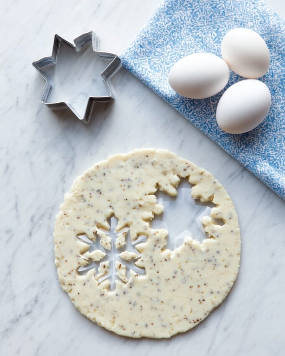 A round, flat dough with two snowflake-shaped cutouts near the center is placed on a white marbled surface. The dough is creamy white with specks of darker bits throughout, indicating spices or seeds mixed in. To the left of the dough, there are two metal cookie cutters—one large star and one smaller snowflake shape. Above them, a folded blue and white patterned cloth holds four white eggs. The whole scene is bright with natural light. Photo taken with an iphone --ar 4:5 --v 7