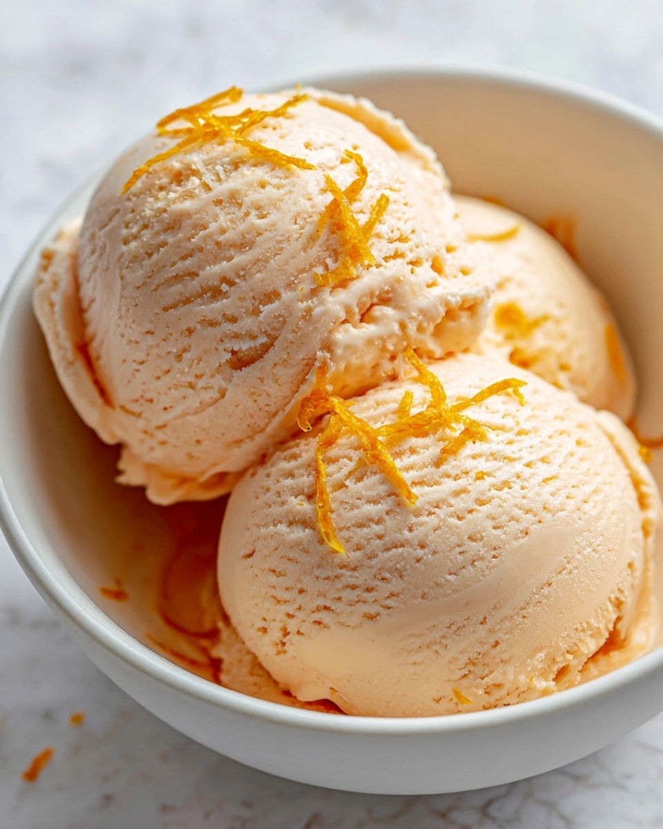 A close-up view of two large scoops of smooth, creamy pale orange ice cream placed side by side in a white bowl, with a few small strands of bright orange zest scattered on top of the front scoop, giving a fresh and textured look. The surface of the ice cream shows fine, slightly rough textures with gentle, soft curves. The background is a white marbled texture. photo taken with an iphone --ar 4:5 --v 7