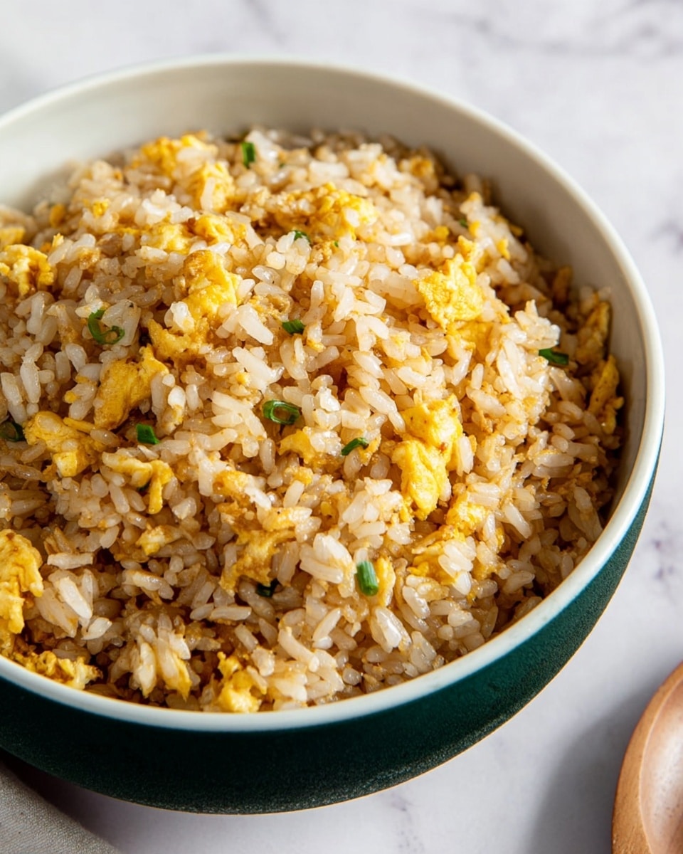 A close-up of a bowl filled with fried rice showing two layers: the base layer is white rice with a slightly oily texture, mixed with small brown browned bits scattered evenly, and the top layer consists of small, irregular pieces of scrambled egg in bright yellow color mixed throughout. The bowl is white on the outside with a dark green interior, placed on a white marbled texture. Soft light highlights the fluffy texture of the rice and the soft scrambled egg pieces. Photo taken with an iphone --ar 4:5 --v 7