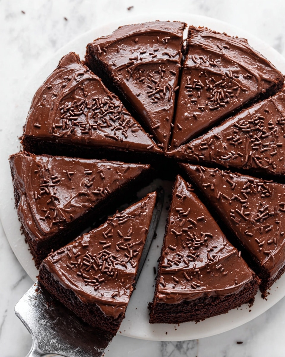 A round chocolate cake is shown on a white marbled surface, cut into six slices with one slice being lifted by a cake server. The cake has two layers: a thick, dark brown chocolate base with a slightly crumbly texture, topped with a smooth, shiny layer of rich chocolate frosting. The top frosting layer is decorated with small, evenly spread chocolate sprinkles. The edges of the cake are clean and the frosting has a glossy, slightly swirled pattern. Photo taken with an iphone --ar 4:5 --v 7