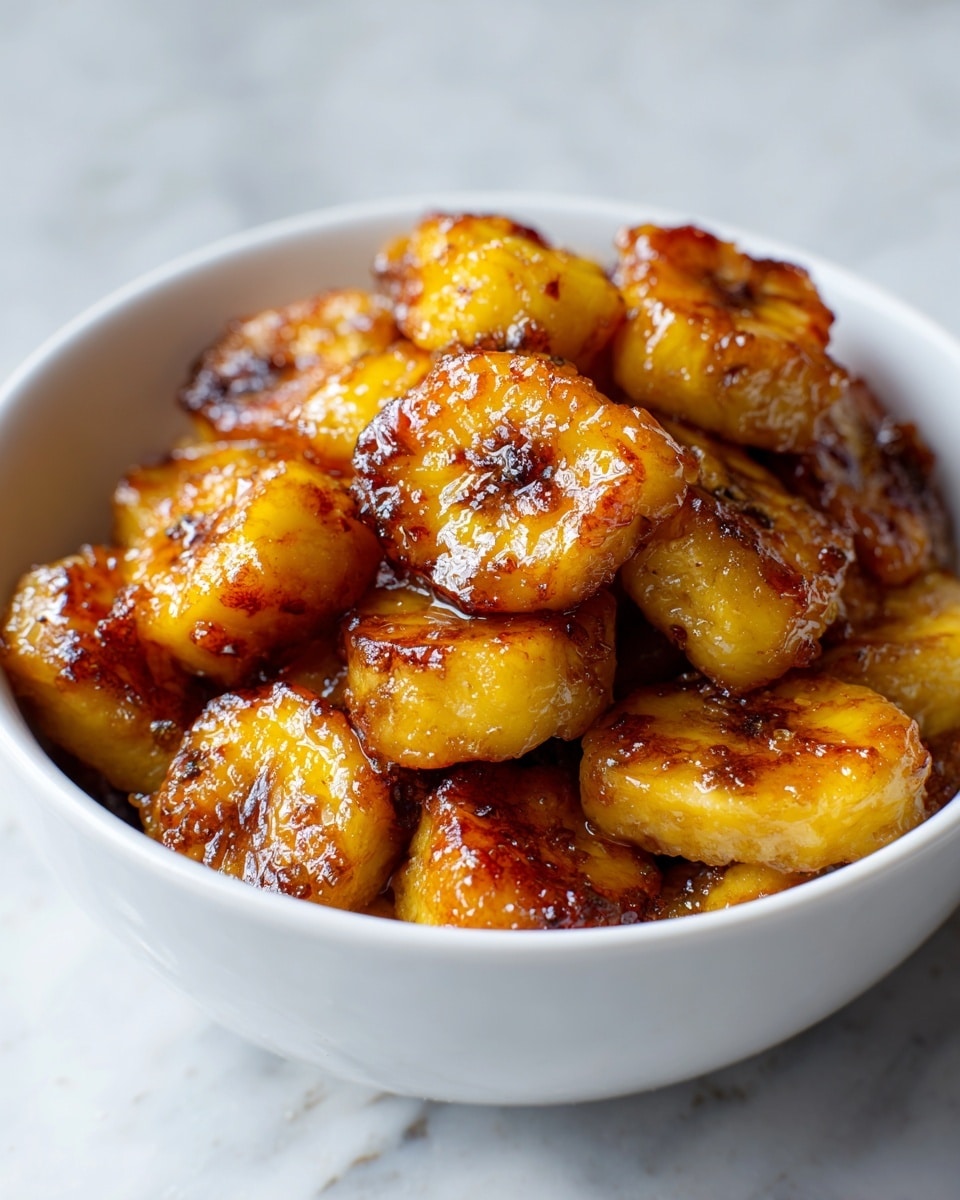 The image shows a white bowl filled with evenly cut golden-brown potato cubes covered in a shiny, thick brown sauce. The potatoes have a slightly crispy texture on the outside with a soft look inside, sitting in a layer of smooth sauce that pools beneath them. The bowl is placed on a white marbled surface, highlighting the warm colors of the dish. Photo taken with an iphone --ar 4:5 --v 7