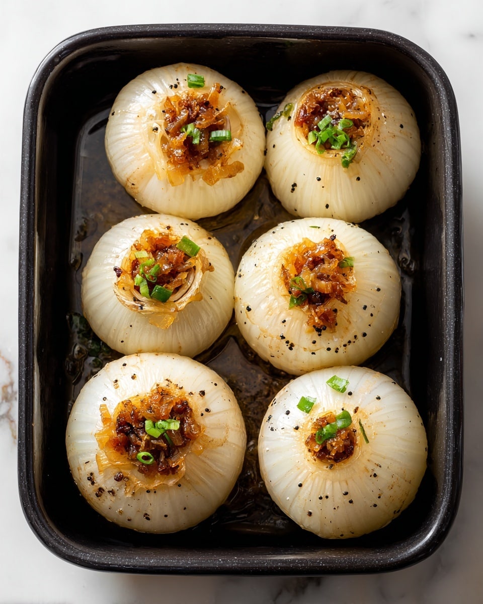 Five round roasted onions with a soft, translucent white outer layer form the base, each hollowed out and filled with a browned, textured mixture of diced cooked onions and small red bits, topped with bright green chopped herbs. The onions are sitting close together in a dark pan with a glossy, oily sheen and small black pepper specks scattered across the surface. The background shows a white marbled texture under soft light, enhancing the warm and cooked appearance of the dish. photo taken with an iphone --ar 4:5 --v 7